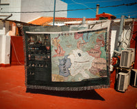 Map-themed blanket draped over a surface with buildings and air conditioning units in the background.